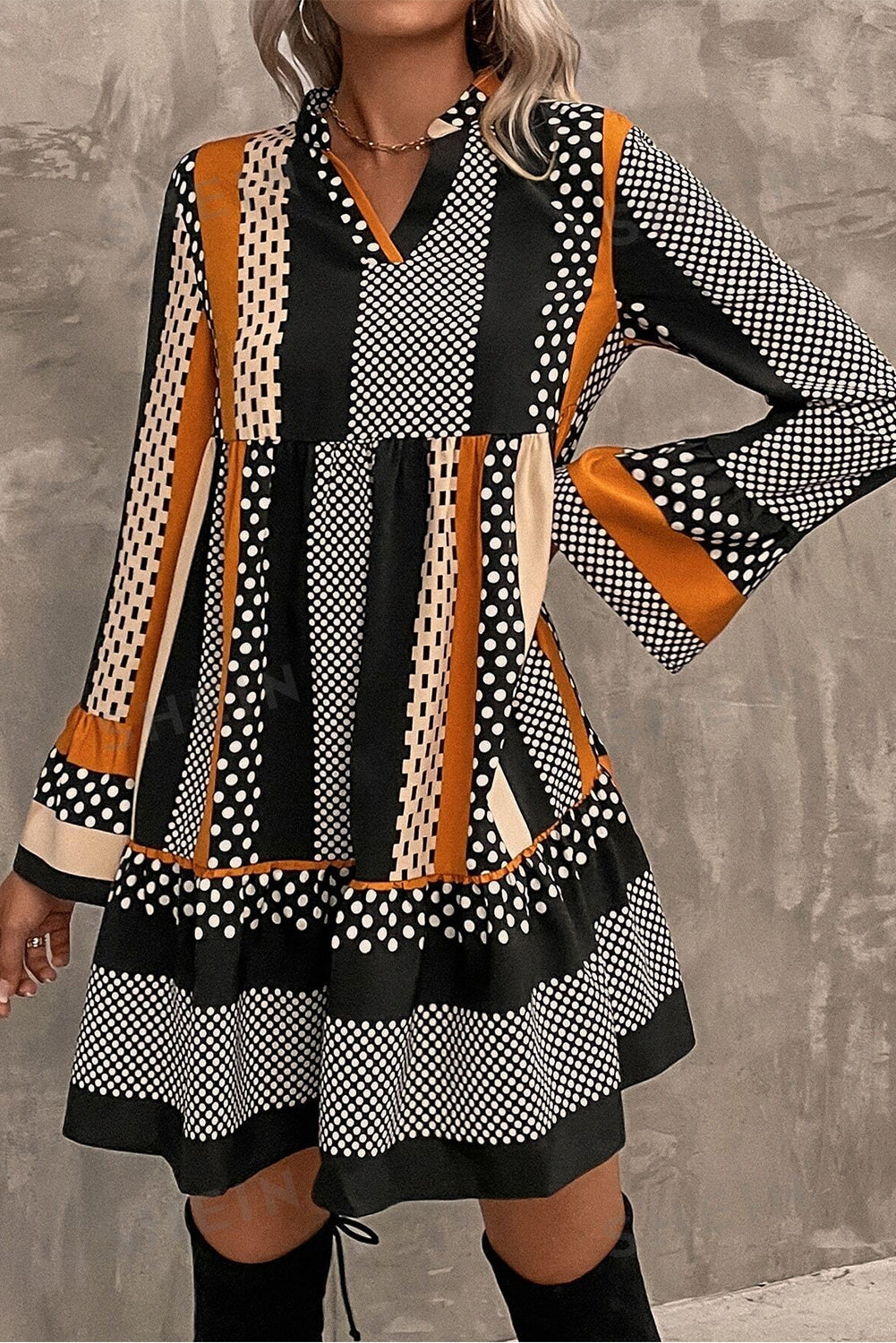 Woman wearing a black striped polka dot print ruffled hem V-neck mini dress with long flared sleeves.