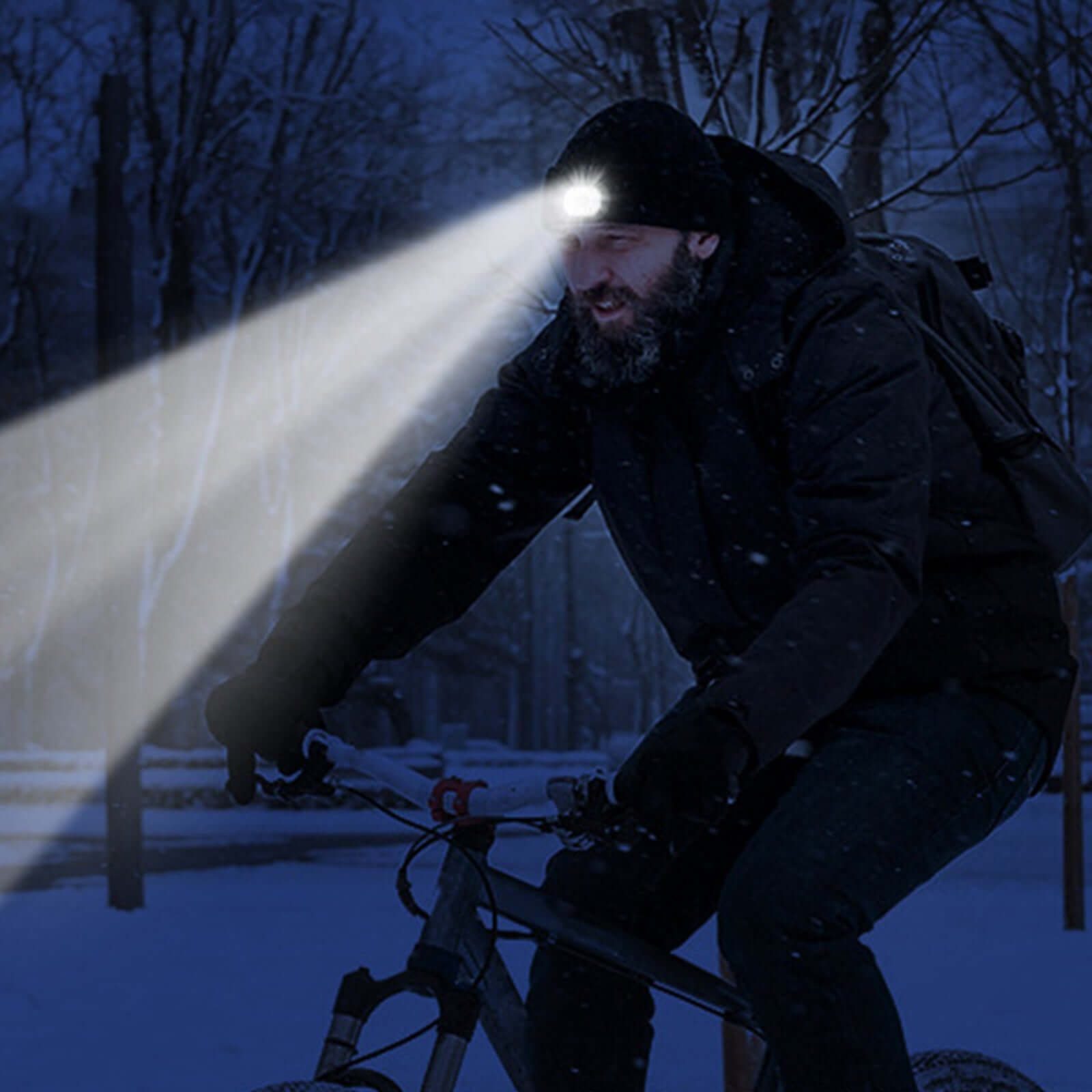 Man cycling at night with LED-lit knit beanie hat in snowy outdoor setting